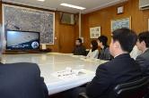 奥に設置された大きなテレビ画面を見ている参加者を後ろから撮影した写真
