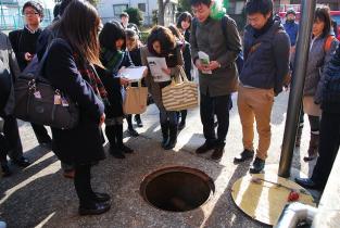 蓋が開いた防火水槽の周りに参加者が集まり中を見ている写真