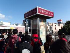 バスの時刻表の上に「習志野文化ホール」と書かれている広告塔の周りに集まっている参加者の写真