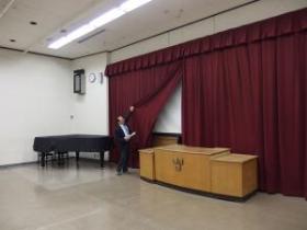 グランドピアノと壇上の間に立っている男性が幕を上げている写真