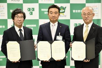 協定書をそれぞれ持ち、大塚隊長、宮本市長、川口副会長が横一列に並んでいる写真