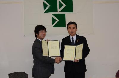 宮本市長と男性が協定書を持ち握手をしている締結式の様子の写真