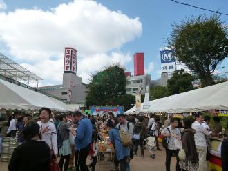 奥にステージがあり通路を挟むように設置された両側のテントの出店に沢山のお客さんが買い物を行っている様子の写真
