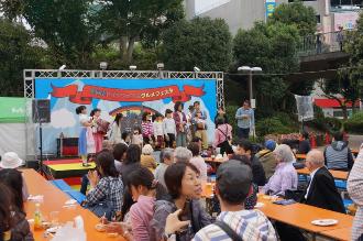 ステージ上に立っている子供たちのイベントステージを席に座って見ているお客さんの写真