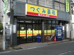 薬局前に自動販売機があり、つぐみ薬局と大きく書かれた看板が設置されたつぐみ薬局の外観写真