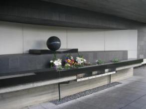 中央に球体の置物があり花が手向けられた参拝広場の写真