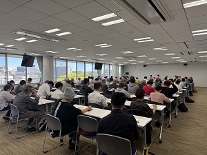 3人掛けの長机が並んでいる部屋で研修会に参加している人達を部屋の後方から写した写真