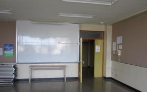 壁際に白板や折りたたまれた長机が収納されている実習室の写真