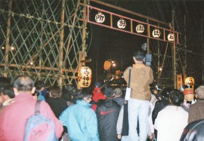 竹矢来で囲まれた磯出御旅所の入り口から中を覗いている人々の後ろ姿の写真