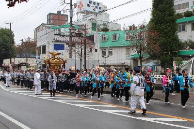 青色の法被を着た人々を先頭に、神輿を担いでいる人々が続いている様子の写真