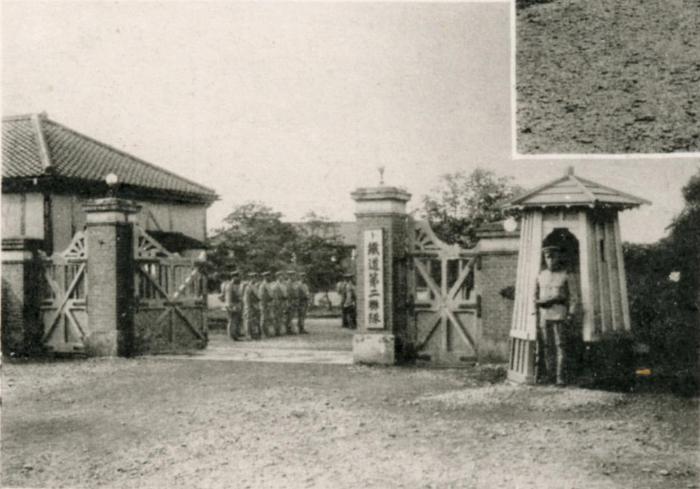 1名の兵士が通用門の門柱横に立ち、鉄道第二連隊の施設前に整列している沢山の兵士の白黒風景写真