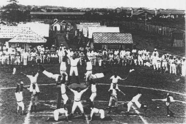 四つんばいになった最下段の演技者の背中の上に両手を広げた演技者が立っている組体操の白黒写真