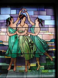 3名の女神が踊っているように描かれている色艶やかなステンドグラスの写真