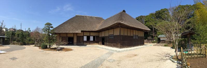 広々とした敷地に青々とした緑の木々が立ち並び、かやぶき屋根をした旧鴇田家住宅の外観写真