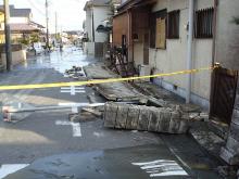 住宅の道路沿いのブロックが道路側に倒れ、道路の至るところが液状化により水溜まりが出来ている液状化被害の写真