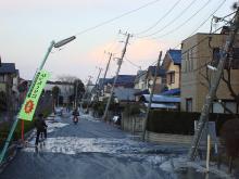 道路沿いに立っている電信柱が斜めに傾き、液状化被害により道路のあちこちに水がでている液状化被害の写真