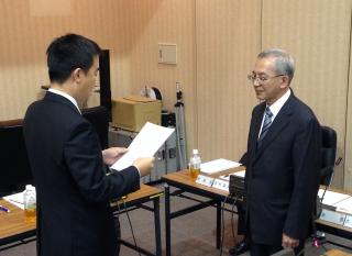 宮本市長と大島会長が向かい合って立ち、宮本市長が諮問書を読み上げている写真