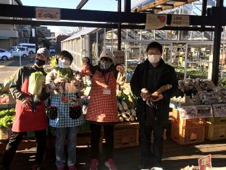 陳列された野菜の前で野菜を持って写っているスタッフ3名と利用者の方の写真