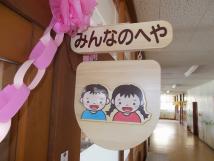 部屋の入り口の木製の板に男の子と女の子の絵が描かれているみんなのへやの写真