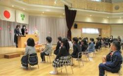間隔をあけて着席している子供達とステージ上の演台前に立っている2名の大人の写真