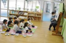 教室の床に整列して座り先生の読み聞かせを真剣に聞いている園児達の写真