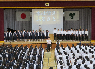 体育館の舞台の上で右に男子生徒、左に女子生徒に分かれて合唱をしている写真