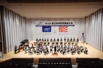 大きな舞台上で指揮者の元、演奏を披露している実花小学校の生徒たちの写真