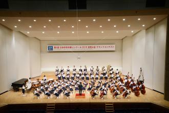 打楽器、弦楽器、管楽器を大きな舞台で演奏している谷津小学校の生徒たちの写真