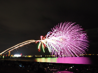 東京湾上空に向かって放たれたピンク色の花火が海面を照らしている写真