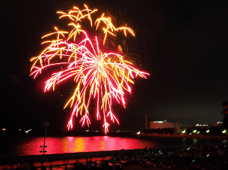 線香花火のような形をした打ち上げ花火が海面を赤色に染めている花火大会の様子の写真