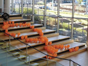 手すりのある木製の階段の上にオレンジ風船でオレンジリボンを表現している様子を上から写した写真