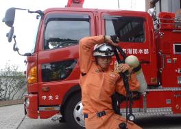 消防車の前でオレンジの消防服を着た木村 勇磨さんの写真
