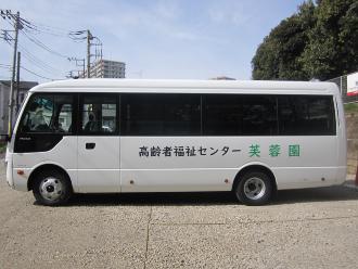 車体に「高齢者福祉センター芙蓉園」と書かれた送迎バスを左側面から撮影した写真