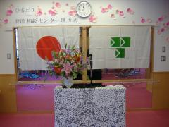 2つの旗が並んで貼られている前に、レースの布で飾られた花が入った花瓶が置いてある壇上を写した写真