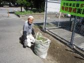 男性が草が入った大きなゴミ袋の横で座っている写真