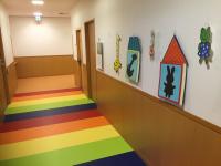 壁にキリンやウサギなどの飾りが飾られ、床がカラフルな色で装飾された廊下の写真