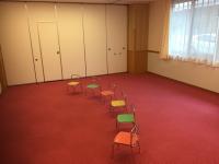 赤い絨毯が敷かれ、子ども用の椅子が6脚並んでいる活動室の写真