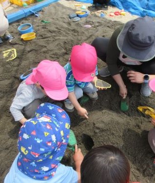 保育者と一緒に山砂場で遊ぶ3歳児