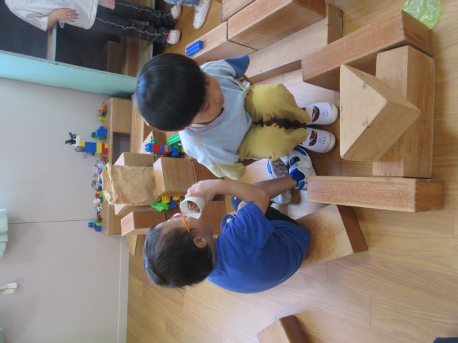 4歳児が大型積み木で乗り物を作り、運転手やジュースを飲んだお客さんが乗っているところ