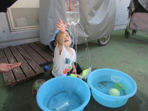 0歳児がペットボトルで作った如雨露の水に手を伸ばして触ろうとしているところ