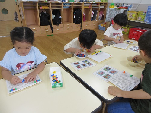 3歳児が、白いボードにカラフルなステッキを指して、絵や模様を作って遊んでいる。