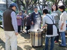 広場でいも煮会方々が大きな鍋炊き出しを行っている様子の写真