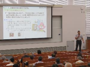 約150名の前でスクリーンに映し出された資料の説明をする危機管理監