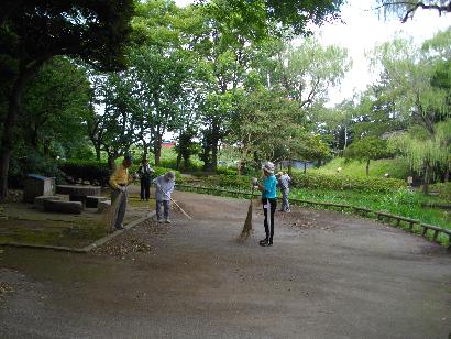 あかしあ会の方々が木々に囲まれた公園を清掃作業している様子の写真