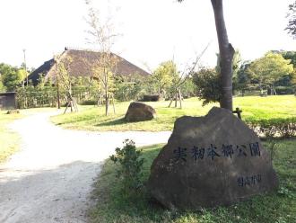 「実籾本郷公園」と刻まれた石碑と広々とした広場の所々に木々が植樹されている実籾本郷公園の写真