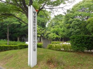 青々とした緑の木々や植木が立ち並んだ秋津公園の広場に文字塔が設置されている写真