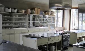 壁に設置された棚に鍋や調理器具が収納されており、調理台が並んでいる調理室の写真
