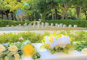秋津公園内にある「平和の広場」に設置された献花台に黄色や白色の花が置かれた写真