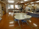 手前側と奥側に丸いテーブルと椅子が置かれ、壁側には棚などが設置された交流コーナー内観の写真