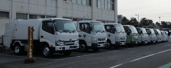 沢山の収集車両が駐車場に横一列に並んで駐車されてい写真